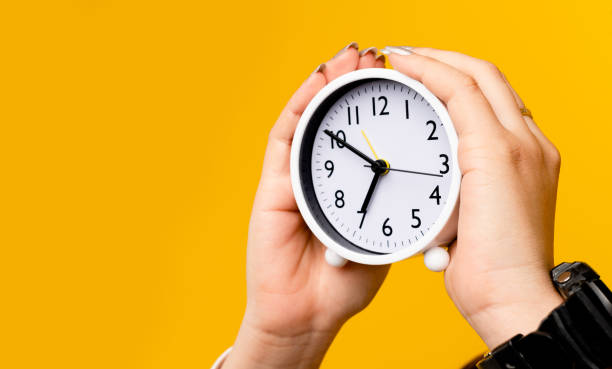 istock Asian woman's hand and white alarm clock on yellow background 1401891442