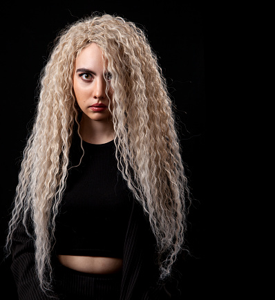 portrait of a young blonde girl with long curly hair in the studio on black background