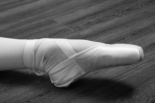 female ballerina feet in pointes on a wooden floor closeup monochrome image