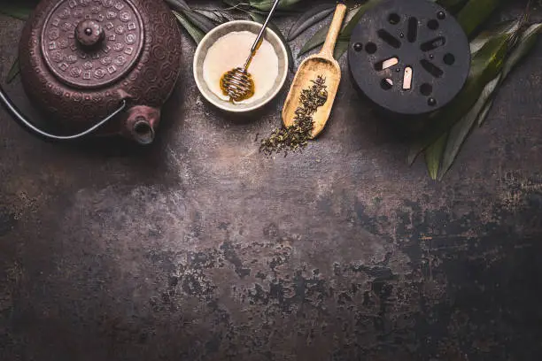 Traditional Asian green tea background with black iron teapot, candle and honey on dark rustic background with copy space, top view