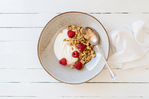Granola with raspberries and yogurt. Beside the plate is a white napkin.
