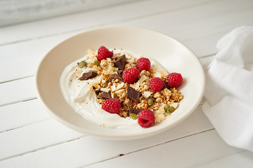 Granola with raspberries, chocolate and curd cheese standing on a white table