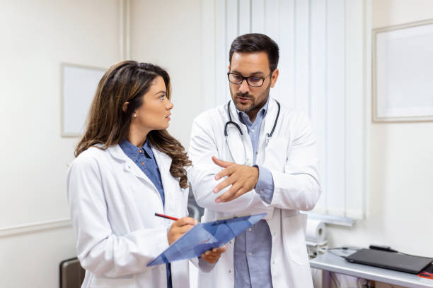 medici che discutono su un referto medico in ospedale. medico di sesso femminile e maschile che controlla il referto clinico del paziente online. personale sanitario che discute in un ufficio di una clinica privata. - physicians assistant foto e immagini stock