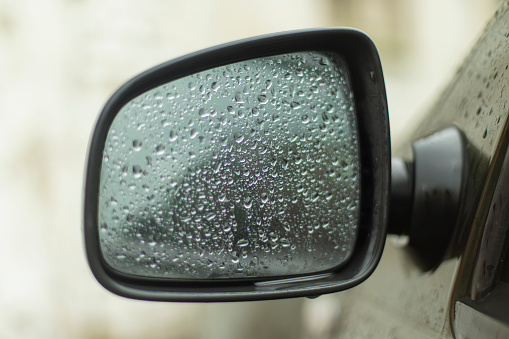 Wet rear-view mirror. Drops on glass. Transport in rain. Wet car.