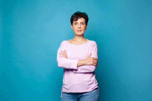 Confident serious mature woman with crossed arms standing against blue studio wall background Confident serious mature woman with crossed arms standing against blue studio wall background 50 59 years stock pictures, royalty-free photos & images