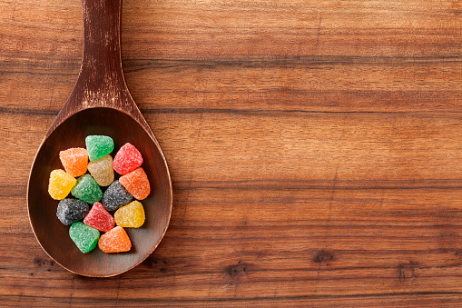 Top view of wooden spoon over table with multi colored gummies on it