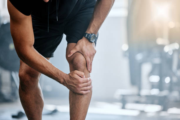 Unknown trainer alone in gym and suffering from knee injury. One coach standing and rubbing leg during workout in exercise health club. One man in fitness centre feeling pain during routine training entrenador desconocido solo en el gimnasio y que sufre de una lesión en la rodilla. un entrenador de pie y frotando la pierna durante el entrenamiento en el club de salud de ejercicios. un hombre en el gimnasio sintiendo dolor durante el entrenamiento de
