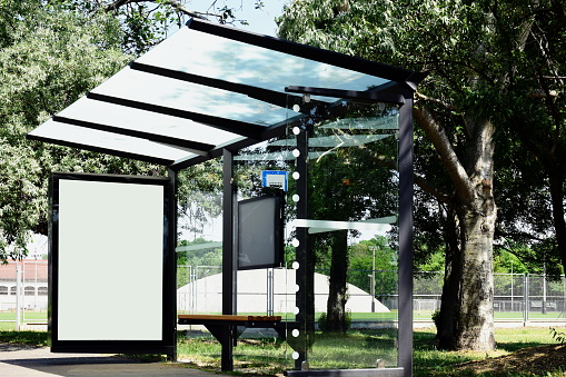 image composite of bus shelter at a bus stop. empty milky white poster ad and advertising display glass and light box. clear safety glass design.  aluminum frame structure. street perspective with trees. green background with trees.