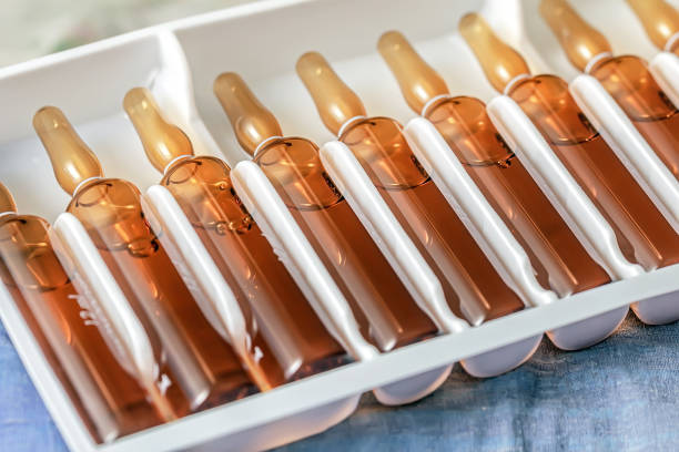 closeup medical ampoules in tray amber glass vials aligned in sterile blister pack, warm reflections on curved surfaces, shallow depth of field, pharmaceutical
