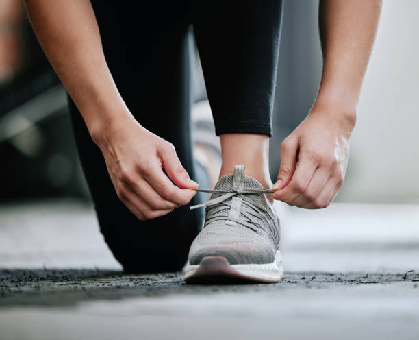 gros plan d’un entraîneur inconnu attachant des lacets seul dans un gymnase. un entraîneur caucasien agenouillé, se préparant à s’entraîner dans un club de santé. femme accroupie dans un centre de conditionnement physique avant l’exercice et l - lace one person vitality action photos et images de collection