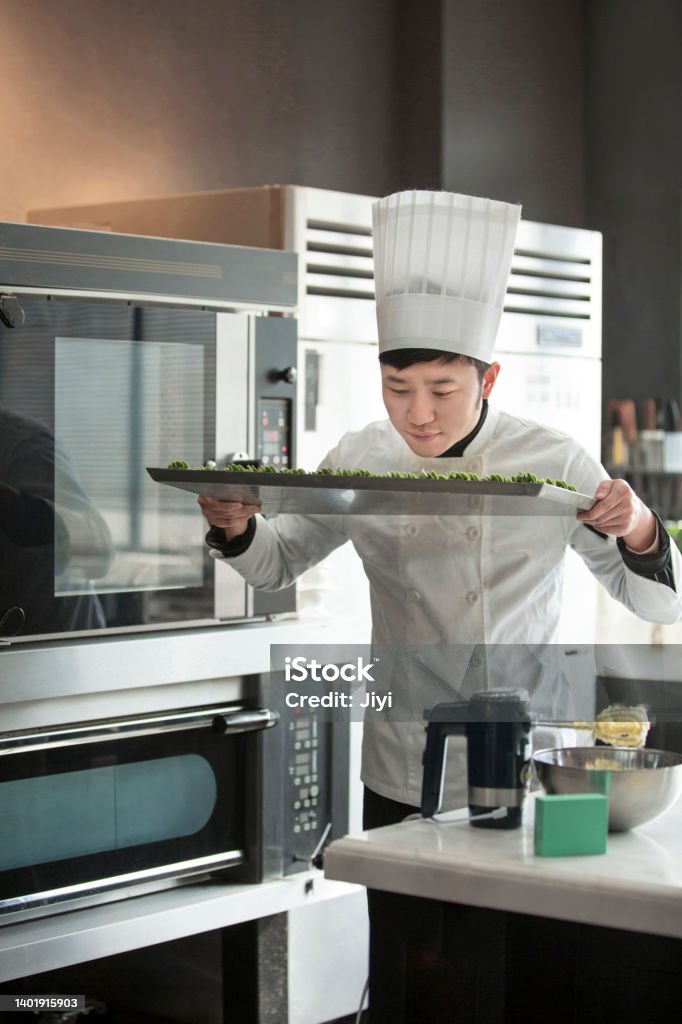 Male Chinese pastry chef smelling matcha cookies before baking them in the oven - stock photo Suitable for sweet delicacies, dessert baking, chef training, catering industry, chef clothing, skill education, nutritious meals, dairy products, wheat products, healthy snacks, baking equipment, commercial kitchenware, kitchen decoration, kitchen electrical equipment, framing technology, Japanese desserts, children's food, hotel back kitchen, print advertising. 20-29 Years Stock Photo