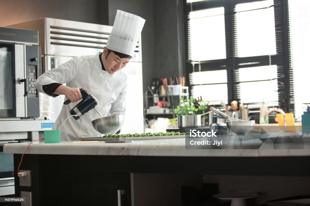 Male Chinese pastry chef making desserts - stock photo Suitable for sweet delicacies, dessert baking, chef training, catering industry, chef clothing, skill education, nutritious meals, dairy products, wheat products, healthy snacks, baking equipment, commercial kitchenware, kitchen decoration, kitchen electrical equipment, framing technology, Japanese desserts, children's food, hotel back kitchen, print advertising. Chef Stock Photo
