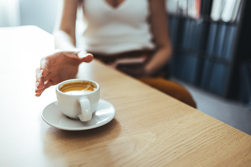 Closeup image of a hand holding a white cup of hot coffee on wooden table in cafe.