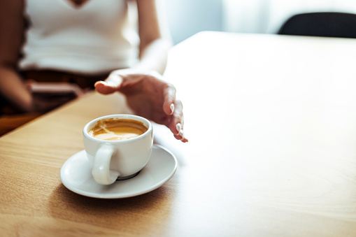 Closeup image of a hand holding a white cup of hot coffee on wooden table in cafe.