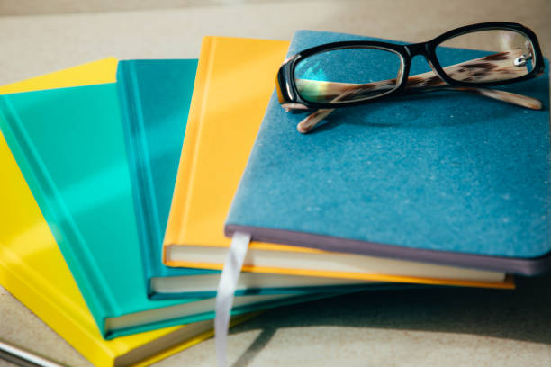 Multi-colored office notebooks on a light beige background and glasses on the top. Set of notebooks, front view
