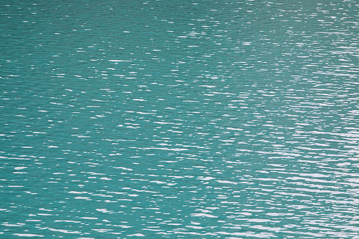 Texture background of turquoise water surface with ripples and light reflections.