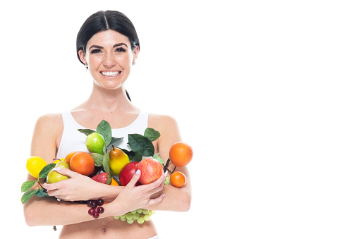 Front view of aged 20-29 years old who is tall person with long hair caucasian young women in front of white background wearing spandex who is smiling and holding fruit with copy space