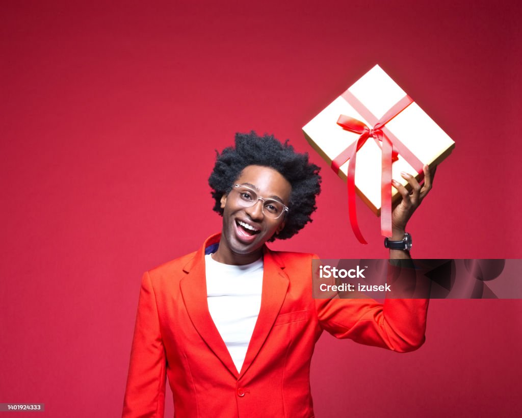 Businessman laughing while holding gift box Portrait of happy businessman holding gift box while standing against red background Gift Box Stock Photo