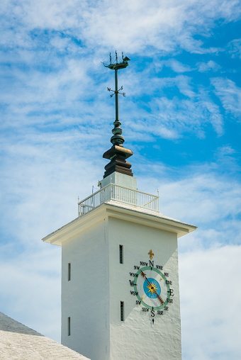 A ship weathervane atop the bright white tower of the City Hall and Arts Center in Hamilton, Bermuda controls the wind direction indicator on the dial below.