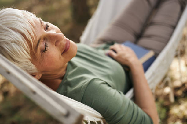 Smiling senior woman taking a nap in hammock. Relaxed mature woman enjoying while taking a nap in hammock outdoors. hammock relaxation women front or back yard stock pictures, royalty-free photos & images