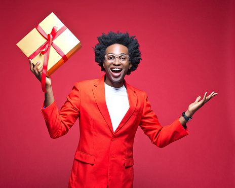Portrait of happy businessman holding gift box while standing against red background