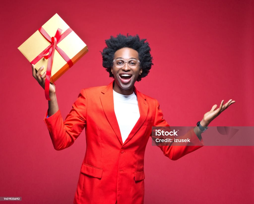 Cheerful businessman holding gift box Portrait of happy businessman holding gift box while standing against red background Birthday Stock Photo