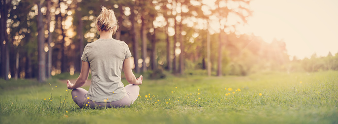 Woman sitting in active wear in lotus position in nature. Concept of healthy lifestyle.
