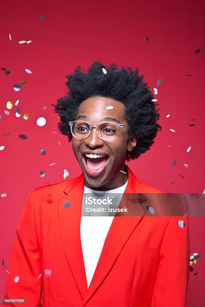 Happy businessman with confetti against red background Cheerful businessman wearing red blazer standing amidst confetti against colored background Party - Social Event Stock Photo