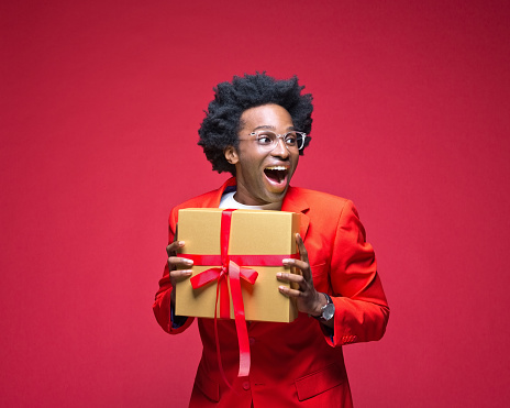 Surprised businessman holding gift box while standing against red background