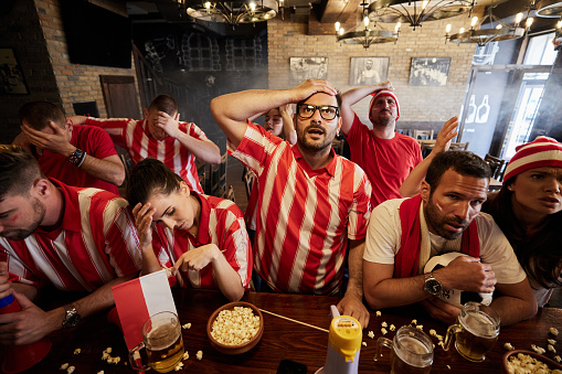 Large group of sports fans feeling displeased after the loss of their favorite soccer team in a pub.