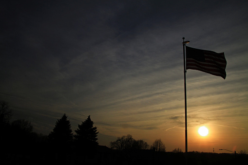 Newington, CT, United States - March 6, 2022: The US flag waves against a cloudy sky on a late Sunday afternoon in Newington, Connecticut. Colors signal the beginning of spring.