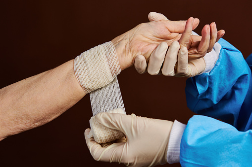 Healthcare worker in gown and latex gloves treats an injury on a senior woman's arm.