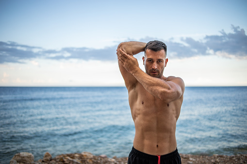 A young handsome man with pronounced muscles exercising on the seashore.