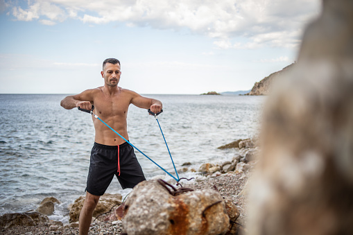 A young handsome man with pronounced muscles exercising on the seashore.