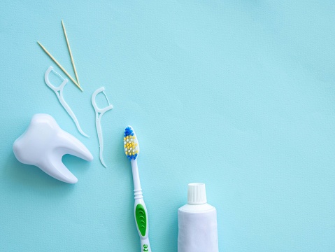 Dental concept of oral hygiene. Dental floss with plastic toothpick, big white tooth, toothpaste and brush. Place for text.