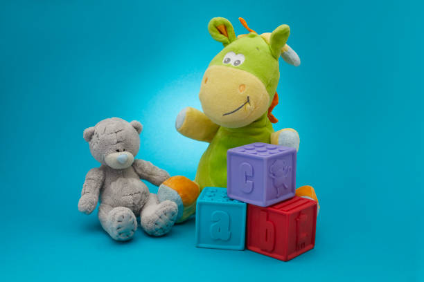 Plush toys bear and dragon siting near Alphabet blocks ABC on blue background.