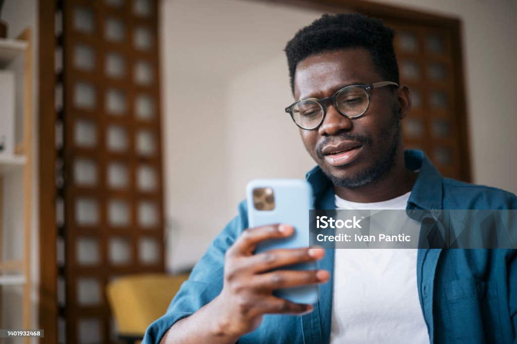 Reading about bad news using a smart phone Young man sitting at home, feeling depressed and trying to contemplate bad news he is reading online using a smart phone Using Phone Stock Photo
