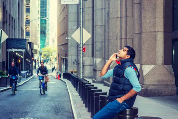 Photo of Young man sitting on street, talking on cell phone in New York City