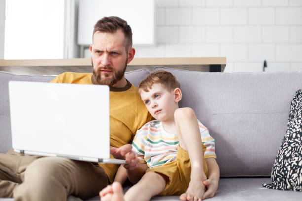 Father and his little son using laptop at home. stock photo