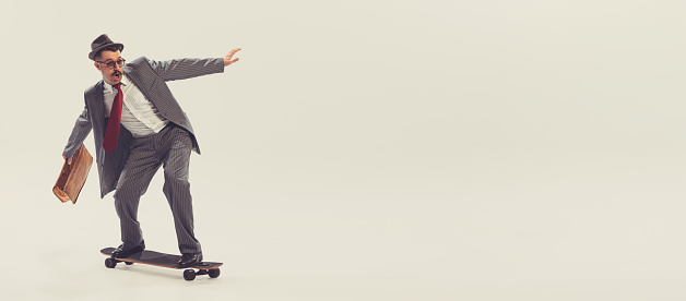 Young funny man, businessman dressed in suit in 50s, 60s fashion style rides skateboard isolated on white background. Concept of modern culture, beauty, ad and fashion. Copy space for ad. Flyer