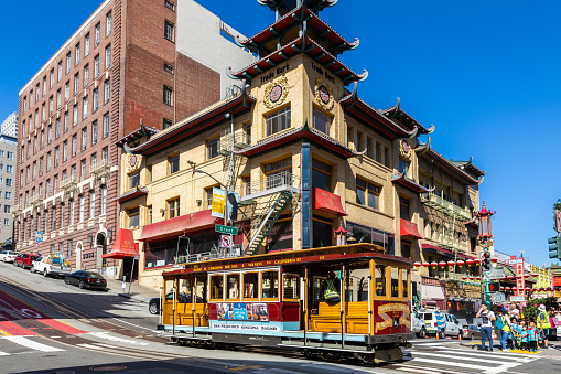 San Francisco, USA - September 27, 2019: Cable car drove through the junction on slope of Chinatown with walking people on crosswalk and background of old chinese style.