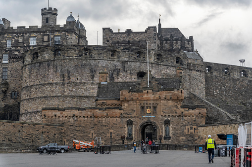 Entrance gate to Edinburgh Castle where tourists are standing, cloudy day.