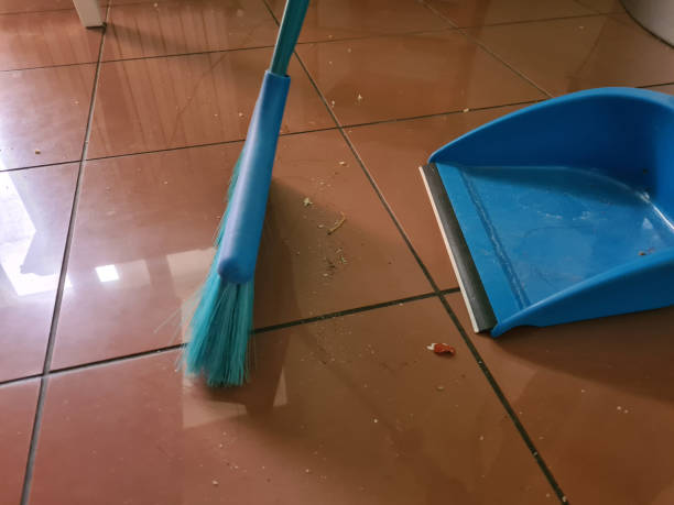 Broom and dustpan on floor with dirt and dust closeup. House cleaning on tiles concept