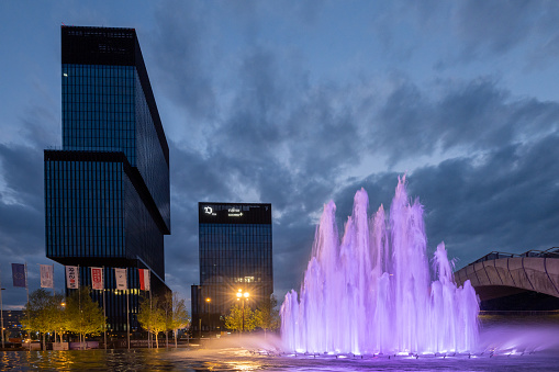 Katowice, Poland - May 8, 2022: illuminated fountains in front of KTW building complex in front of Katowice skyline at sunset hour