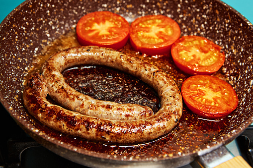 Boerewors and tomatoes browning in a frying pan.