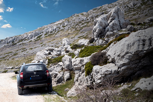 Sveti Rok, Croatia, May 1, 2022: Black off-road vehicle next to slope with large limestone boulders in Velebit mountains