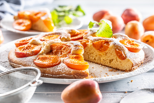 Apricot pie on a white plate, apricots, mint and powdered sugar on the kitchen table.