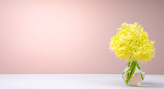 Bouquet of little yellow flowers in a glass vase on the table on a pink background.