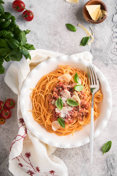 Pasta spaghetti Bolognese. Tasty appetizing italian spaghetti with bolognese sauce, tomato sauce, cheese parmesan and basil on white plate on grey stone or concrete table background. Top view. stock photo