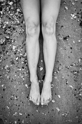 Black and white image of a young woman's legs and feet on a sandy beach with shells in Florida